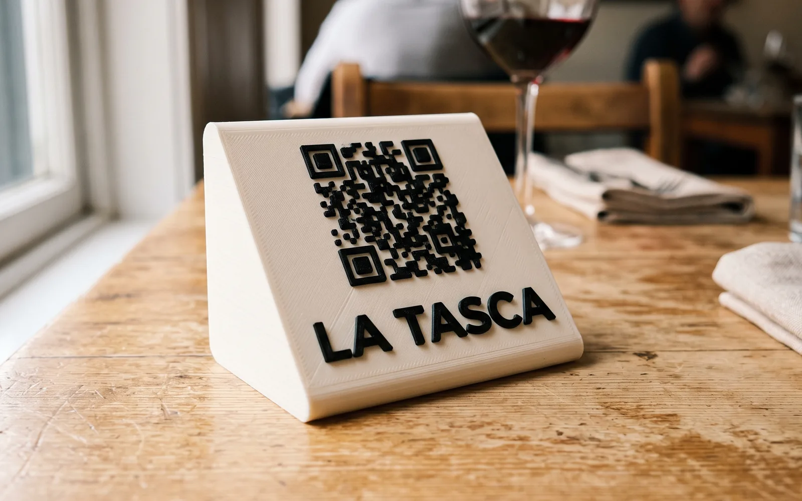 Soporte de sobremesa impreso en 3D con un código QR en relieve negro sobre base color hueso, en la mesa de un restaurante