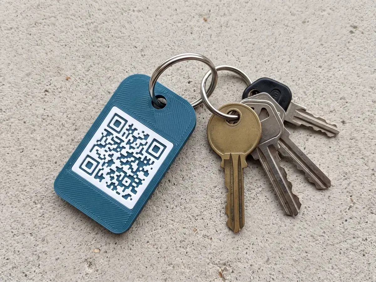 Llavero impreso en 3D con un código QR en relieve, junto a un juego de llaves